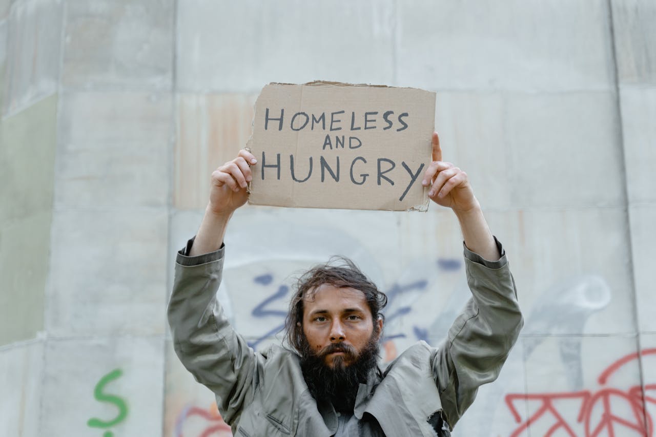 about-us A homeless man holds a cardboard sign reading 'Homeless and Hungry.'