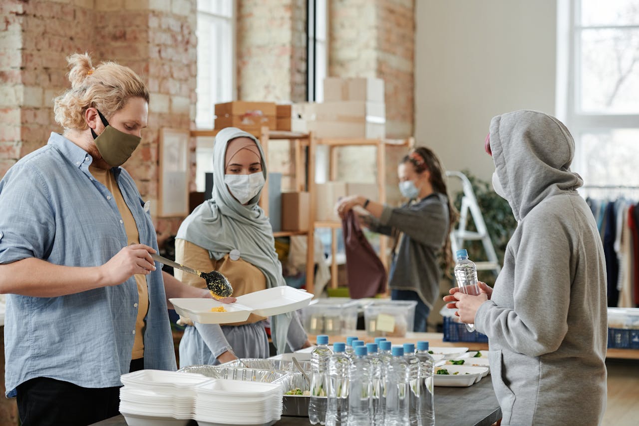 A diverse group of volunteers prepare and distribute food and drinks at an indoor community center.
